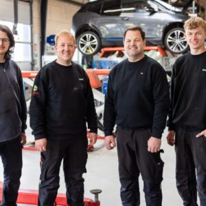 Fire automekanikere foran bil på lift i værksted